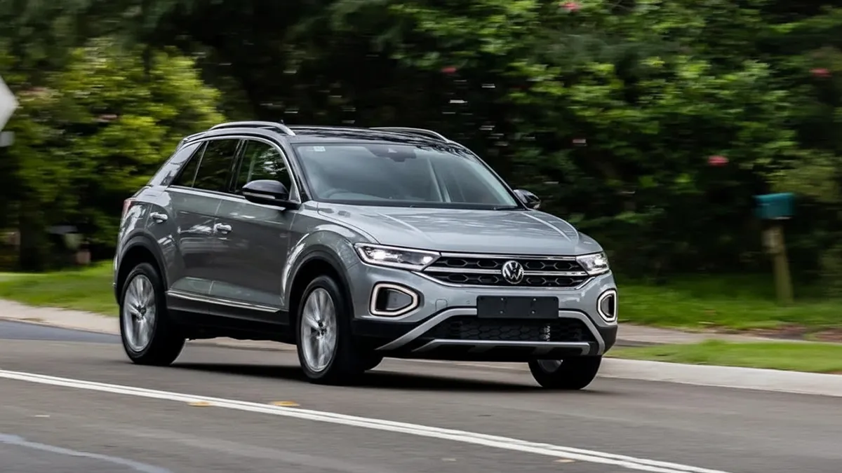 Vue extérieure d’un Volkswagen T-roc roulant sur une route de montagne sinueuse au Maroc, avec un affichage tête haute apparent sur le pare-brise, sans texte ni chiffres. T-roc
