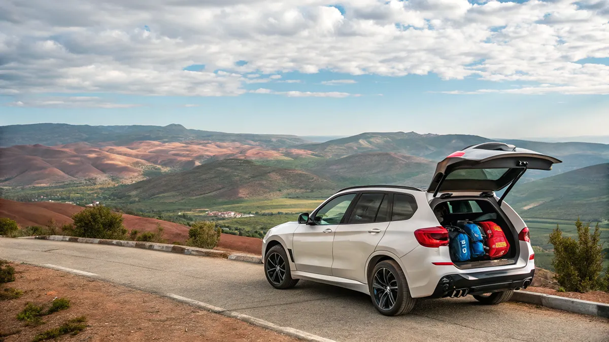 BMW X3 Pack M roulant sur une piste désertique près d'Agadir, avec une kasbah traditionnelle au loin, ciel bleu et lumière vive.