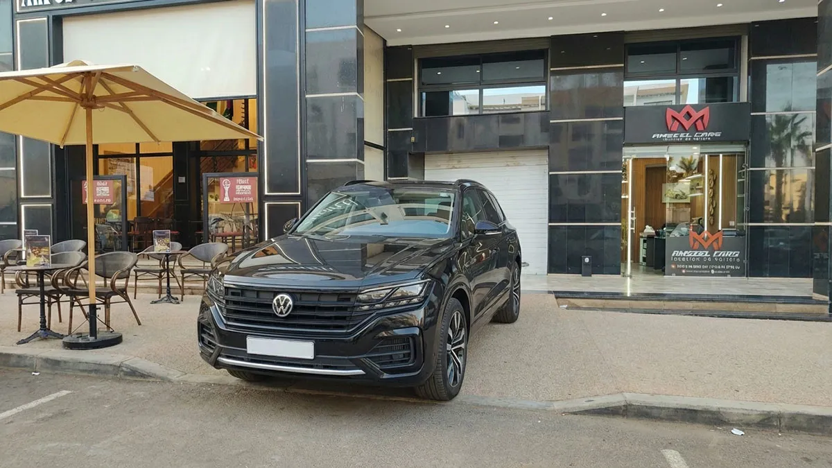 Comptoir d’accueil de l’agence Amseelcars à Agadir avec une Volkswagen Touareg 2025 noire prête à être louée devant la vitrine.