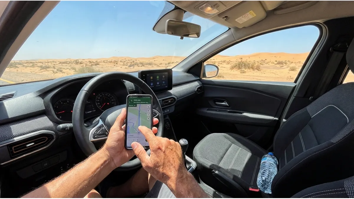 Conducteur dans une Dacia Logan 2024 consultant un GPS sur smartphone avec une bouteille d'eau posée sur le siège passager et paysage désertique visible à travers la vitre, illustrant les conseils de voyage en Dacia Logan