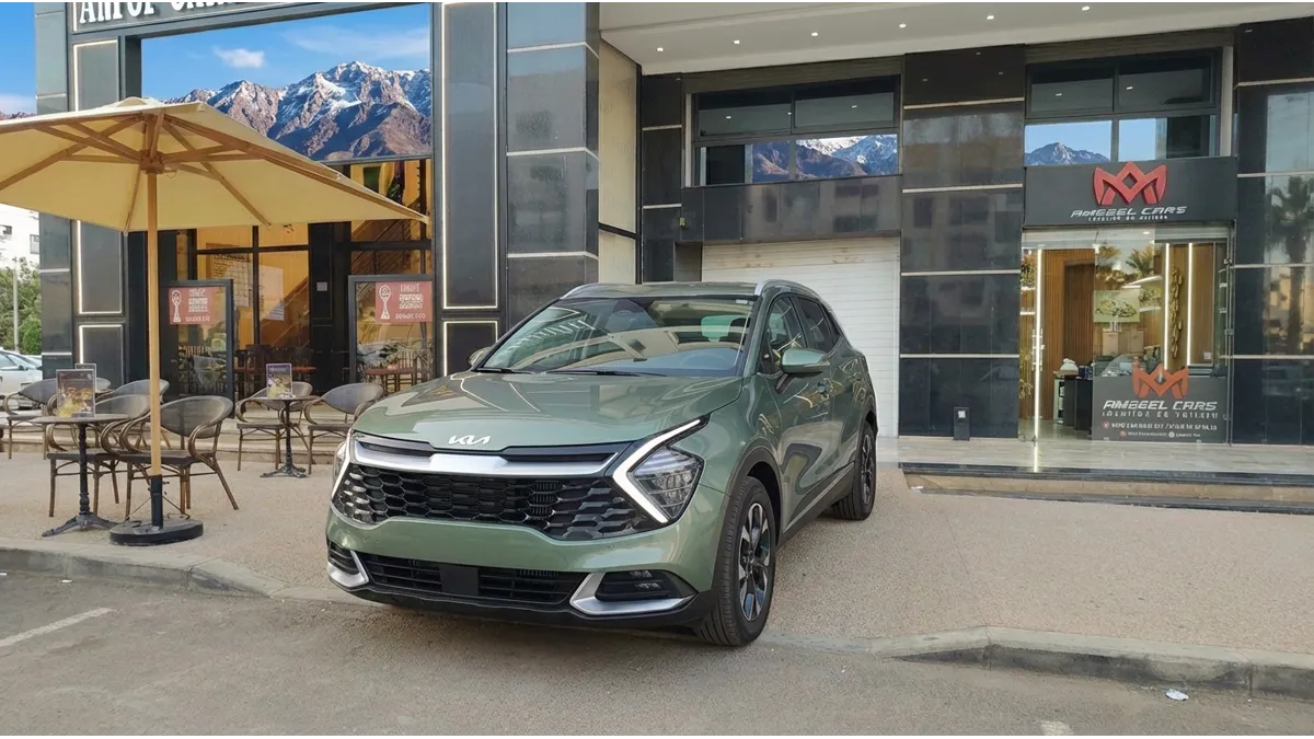 Une voiture de location devant l’agence Amseel Cars à Agadir, prête pour un road-trip au Maroc, avec un paysage montagneux en arrière-plan, illustrant la fiabilité et l’entretien automobile avant le départ