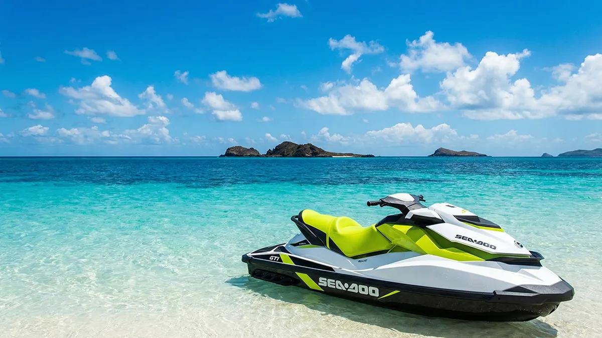 Jet ski posé sur le sable doré d'une plage d'Agadir, moniteur en gilet de sécurité, arrière-plan sur le port de plaisance et la corniche, illustrant l’accès et la sécurité pour le jet ski