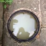 Blocked outdoor drain with standing dirty water, showing an overflow problem.