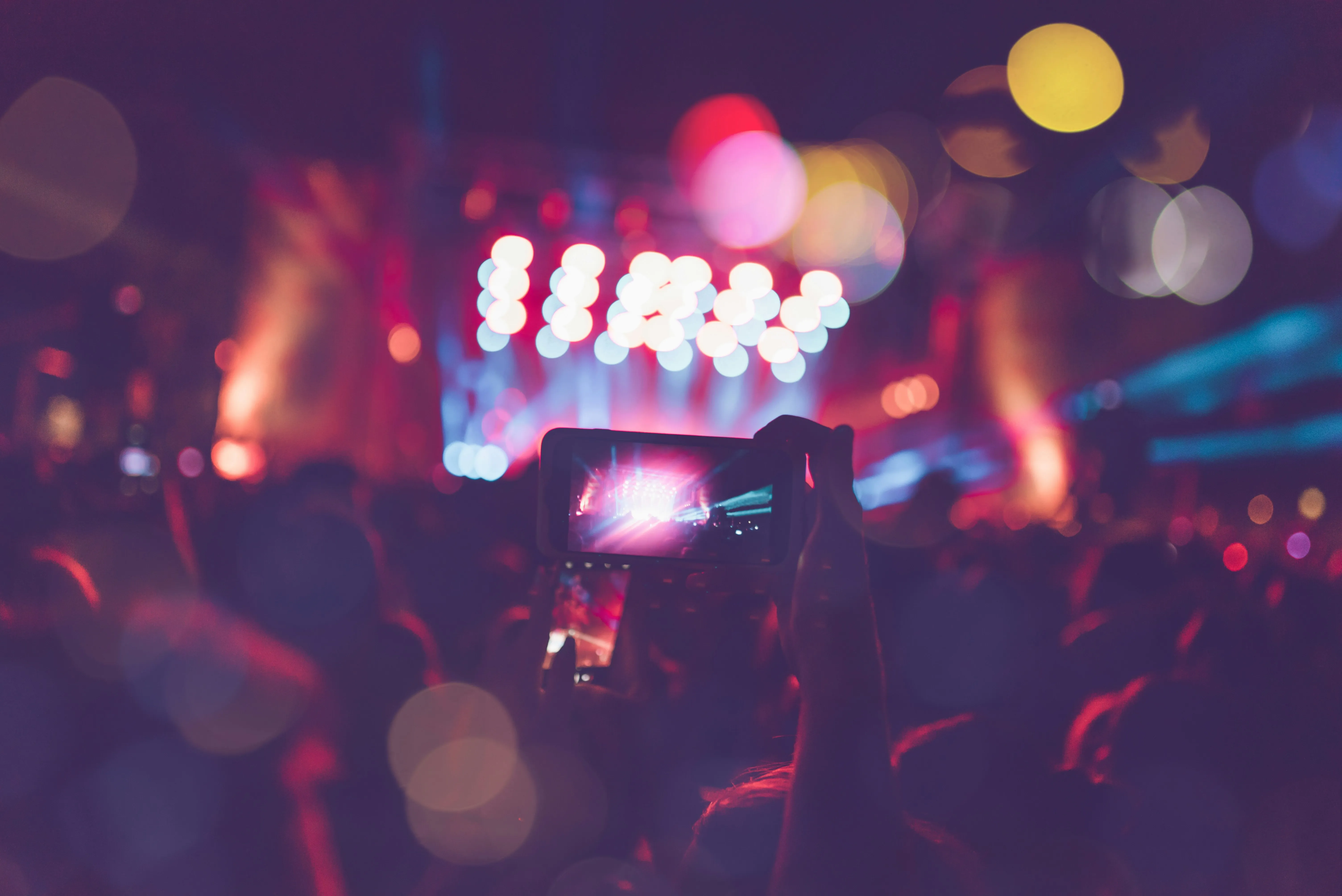 Crowd at a lively event, capturing colourful stage lights with a smartphone, showing an unforgettable party atmosphere.