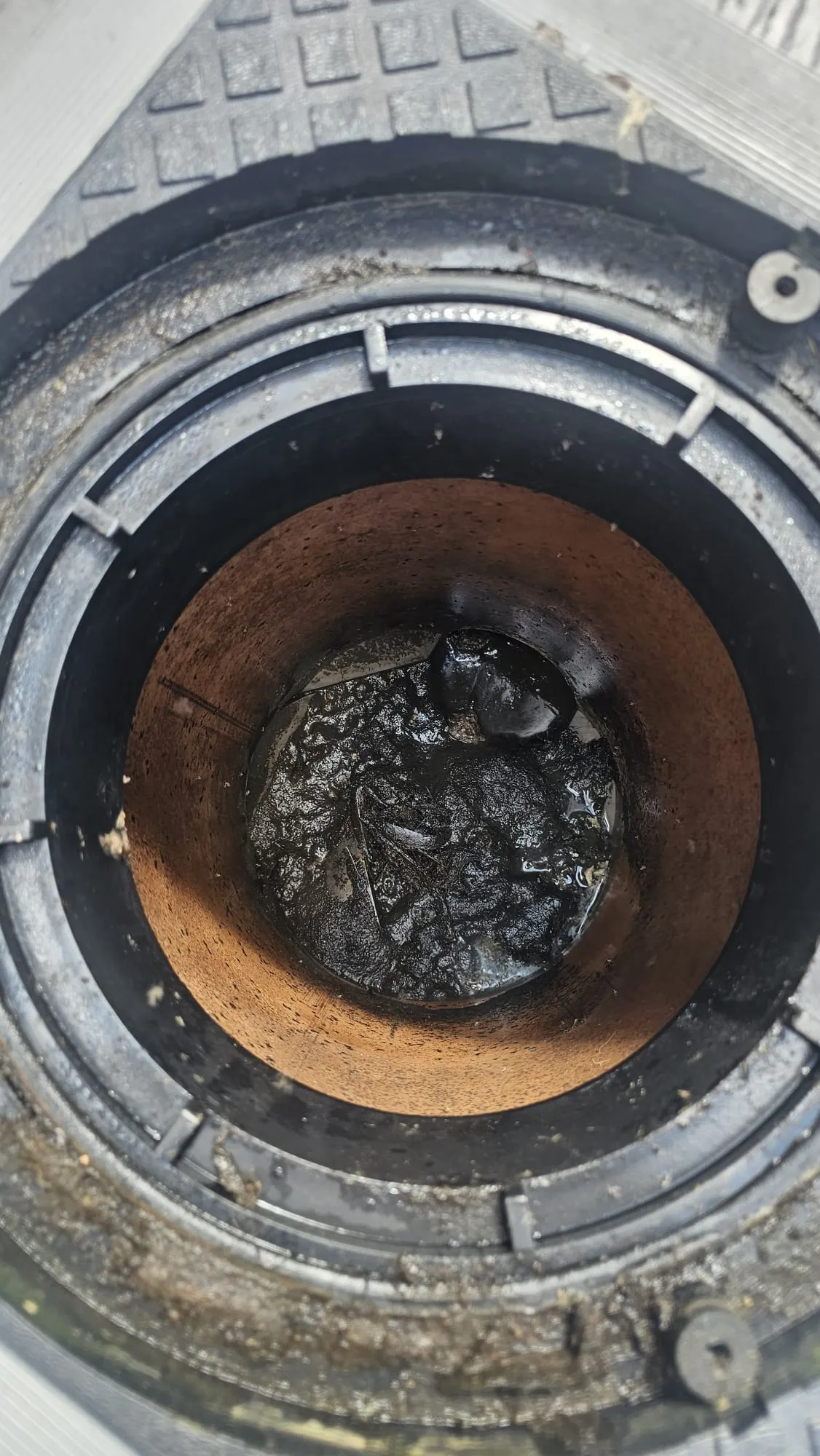 Close-up view of a severely blocked drain opening, revealing thick, dark sludge and debris preventing water flow.