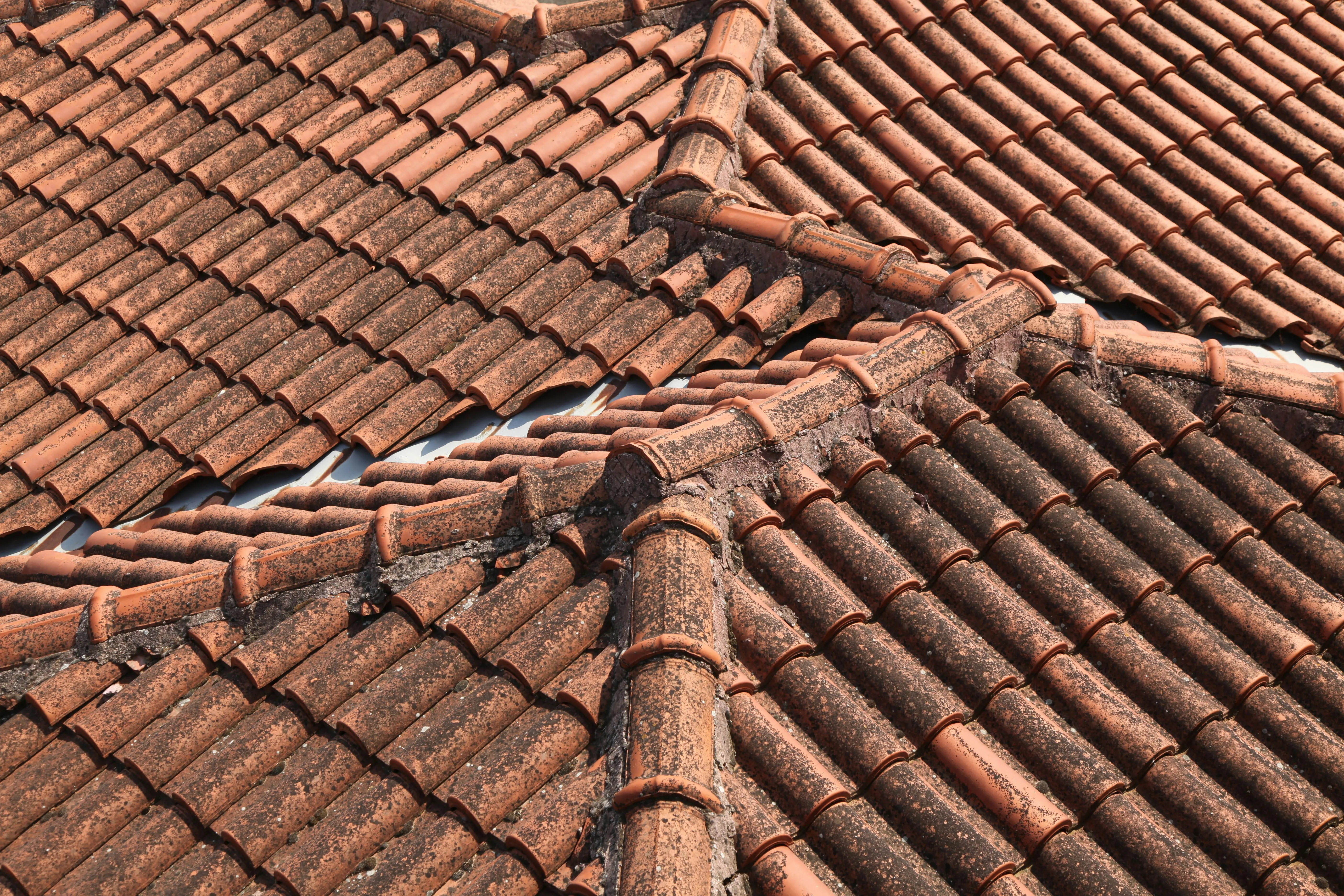 Close-up of an old terracotta tiled roof with visible moss, dirt, and wear, suggesting a need for professional roof cleaning, maintenance, or repair.