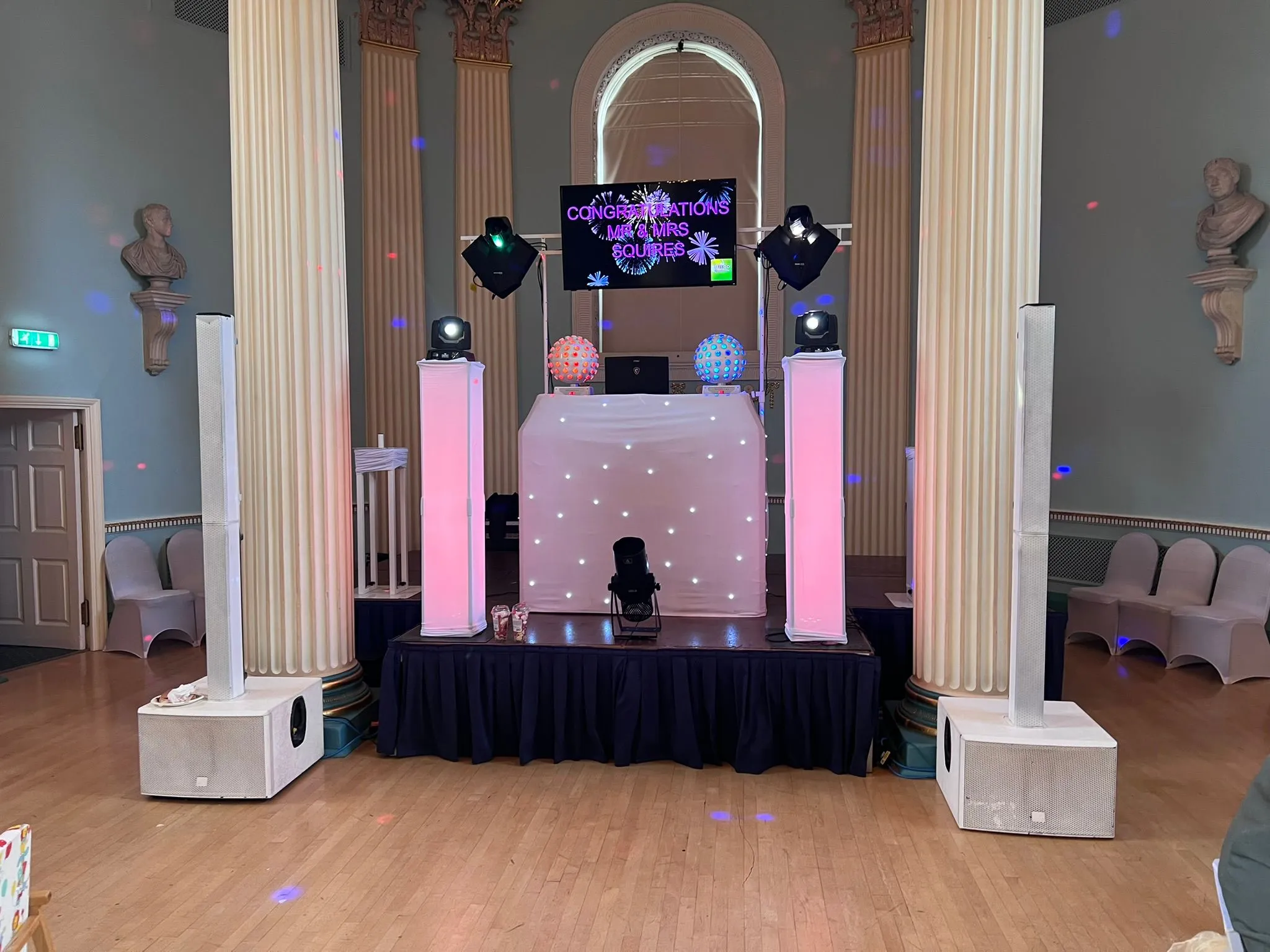 Professional wedding DJ setup with LED screen displaying a 'Congratulations' message, a star-lit booth, tall speakers, and pink uplighting in a grand hall.