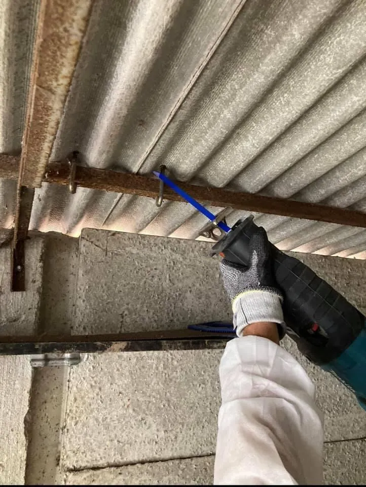 A professional using a reciprocating saw to cut an asbestos cement roof