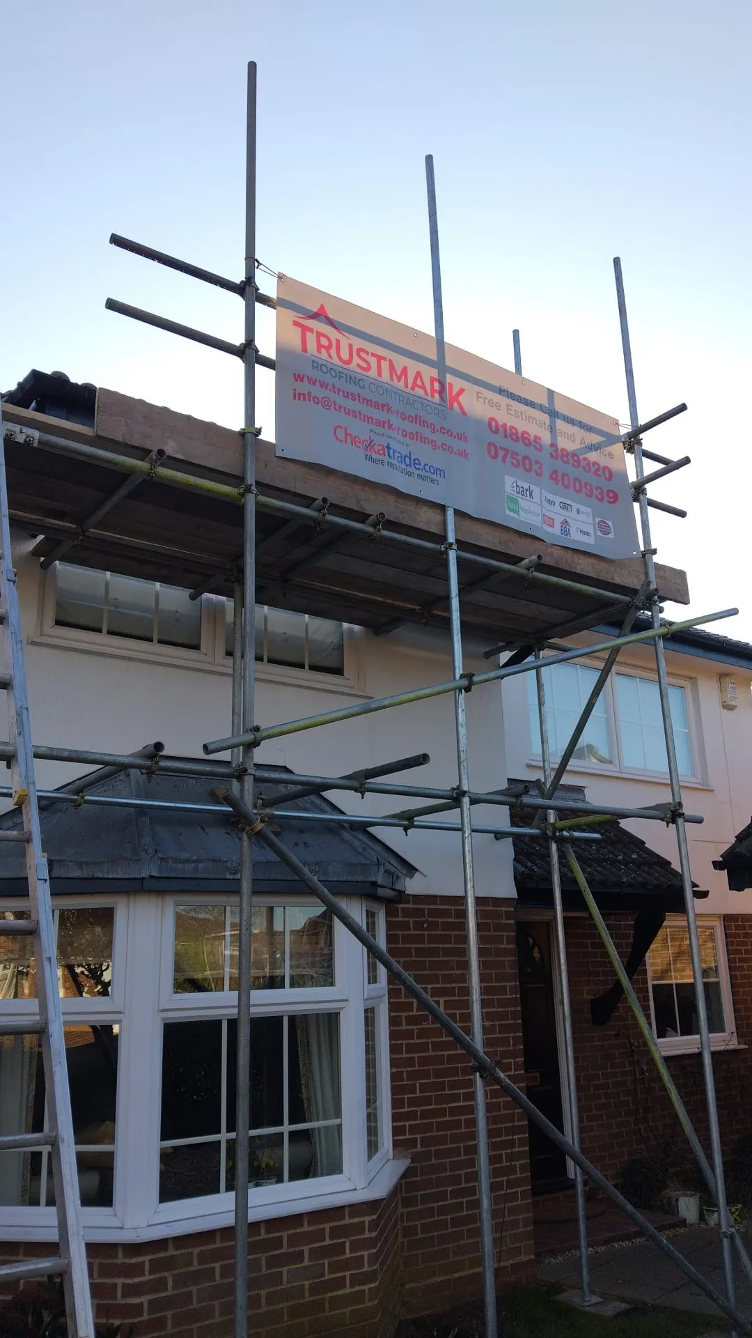 Scaffolding around a house with a Trustmark Roofing banner visible, ready for roof work.
