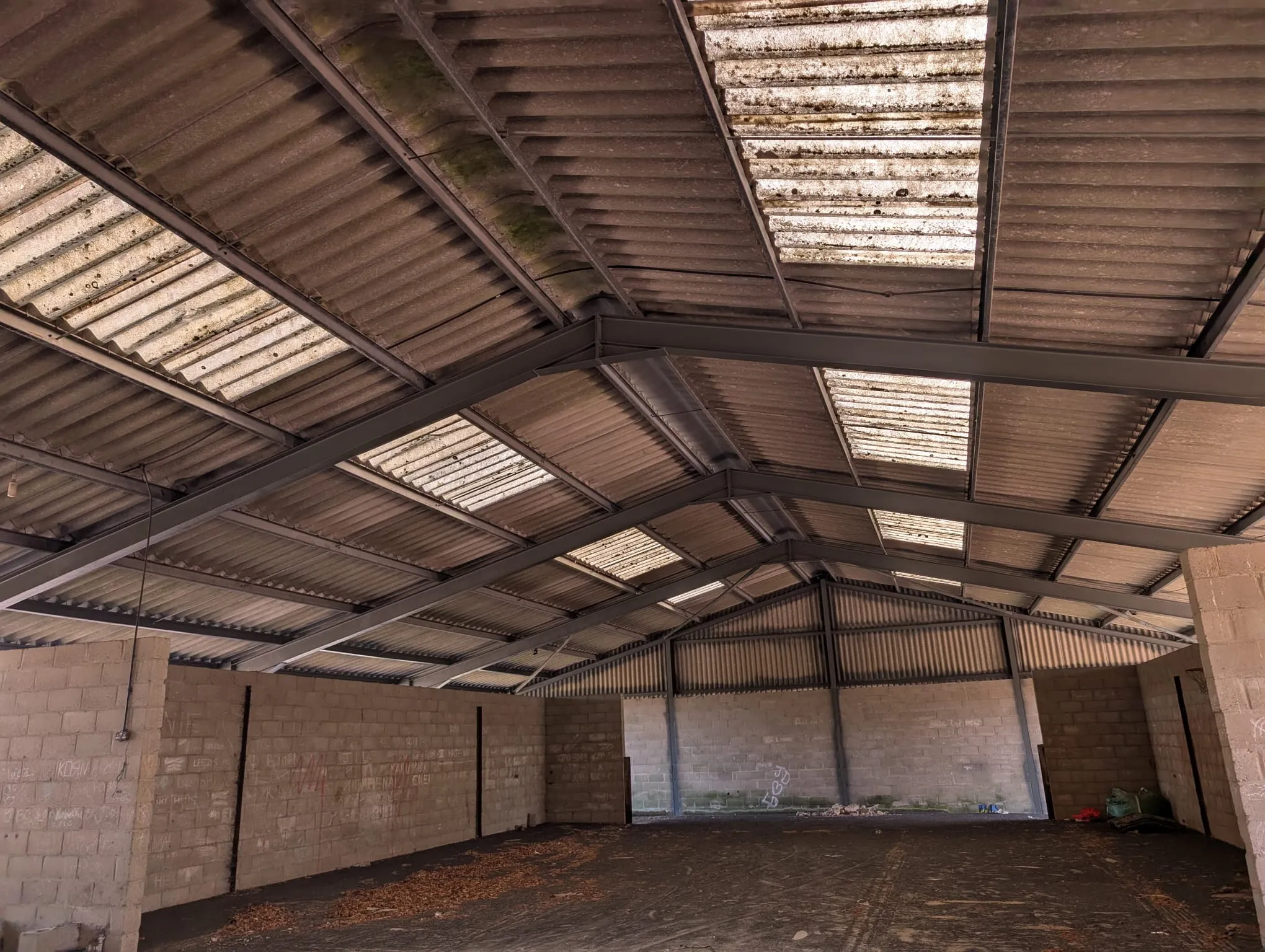 Interior of a large industrial building with an old, corrugated asbestos cement roof and exposed metal supports.