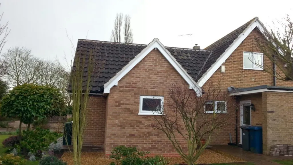 A residential house featuring a dark tiled pitched roof with white fascias and gutters, showcasing a typical property serviced by Bridgeford Roofing.
