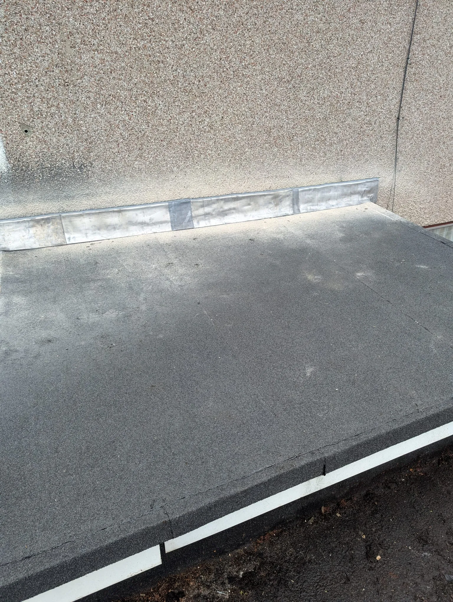 A close-up view of a new flat felt roof installation with lead flashing and a white fascia board.