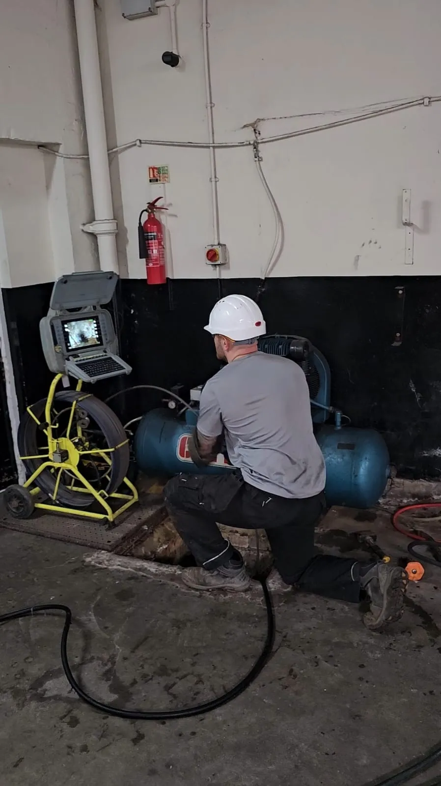 A drainage engineer conducting a CCTV drain inspection with camera equipment in a commercial building.