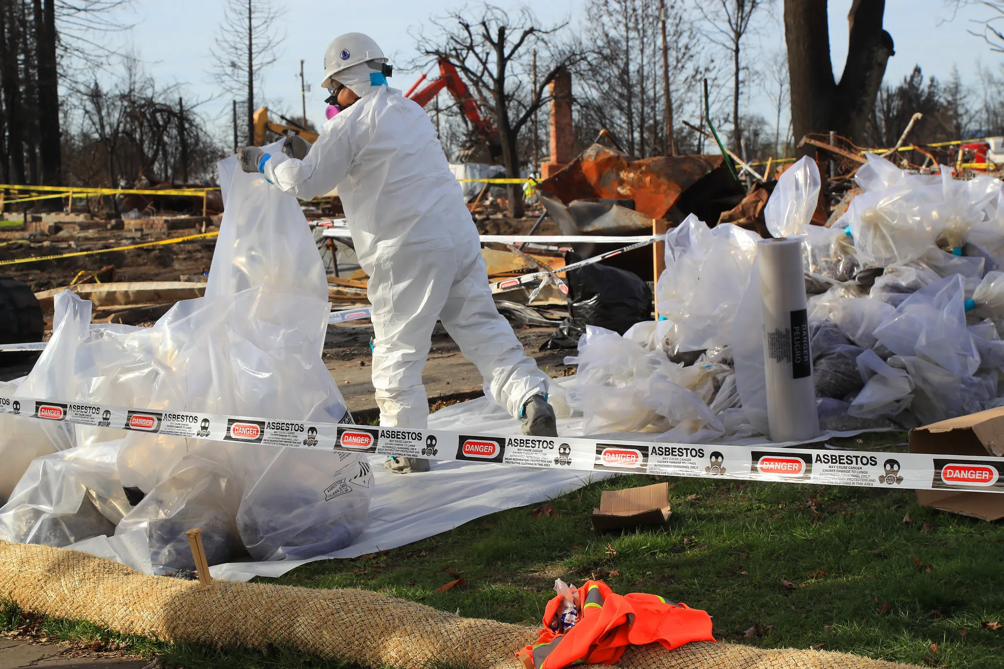 Asbestos removal worker in protective suit handling hazardous waste bags