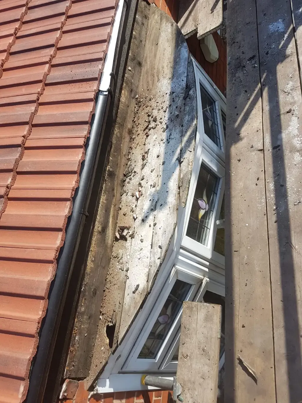 Damaged roofline fascia and guttering above a bay window during repair in Manchester