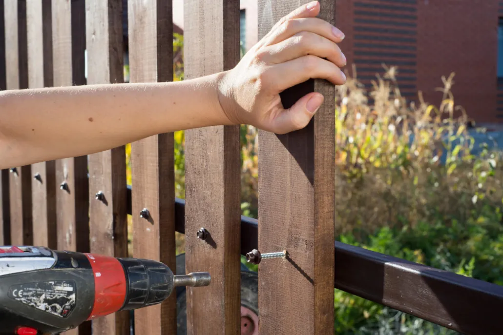 Hand using a drill to screw in a wooden fence panel during installation