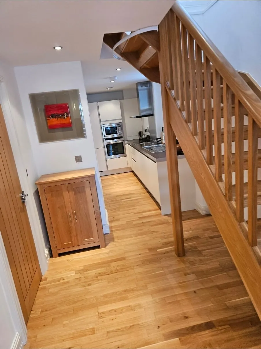 Modern house interior with wooden stairs, a contemporary kitchen, and light wooden flooring, ideal for house clearance services.