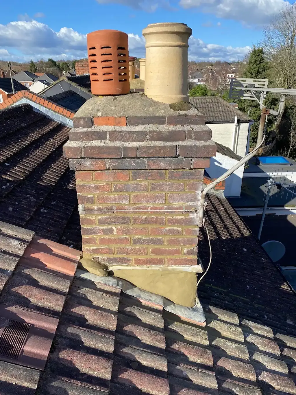 A close-up of a chimney stack on a tiled house roof with pots and lead flashing.