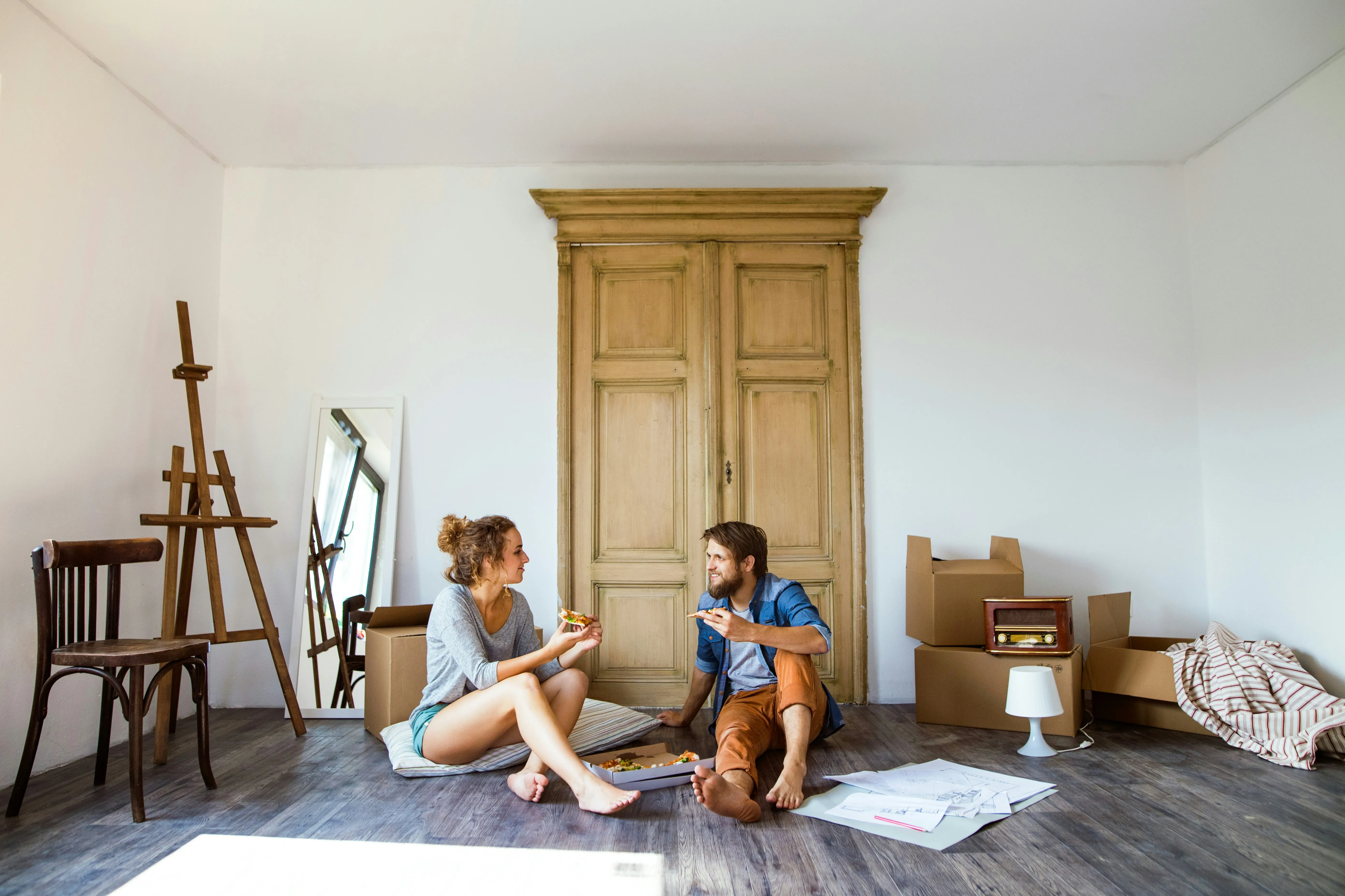 Couple eating pizza on floor surrounded by moving boxes after a move
