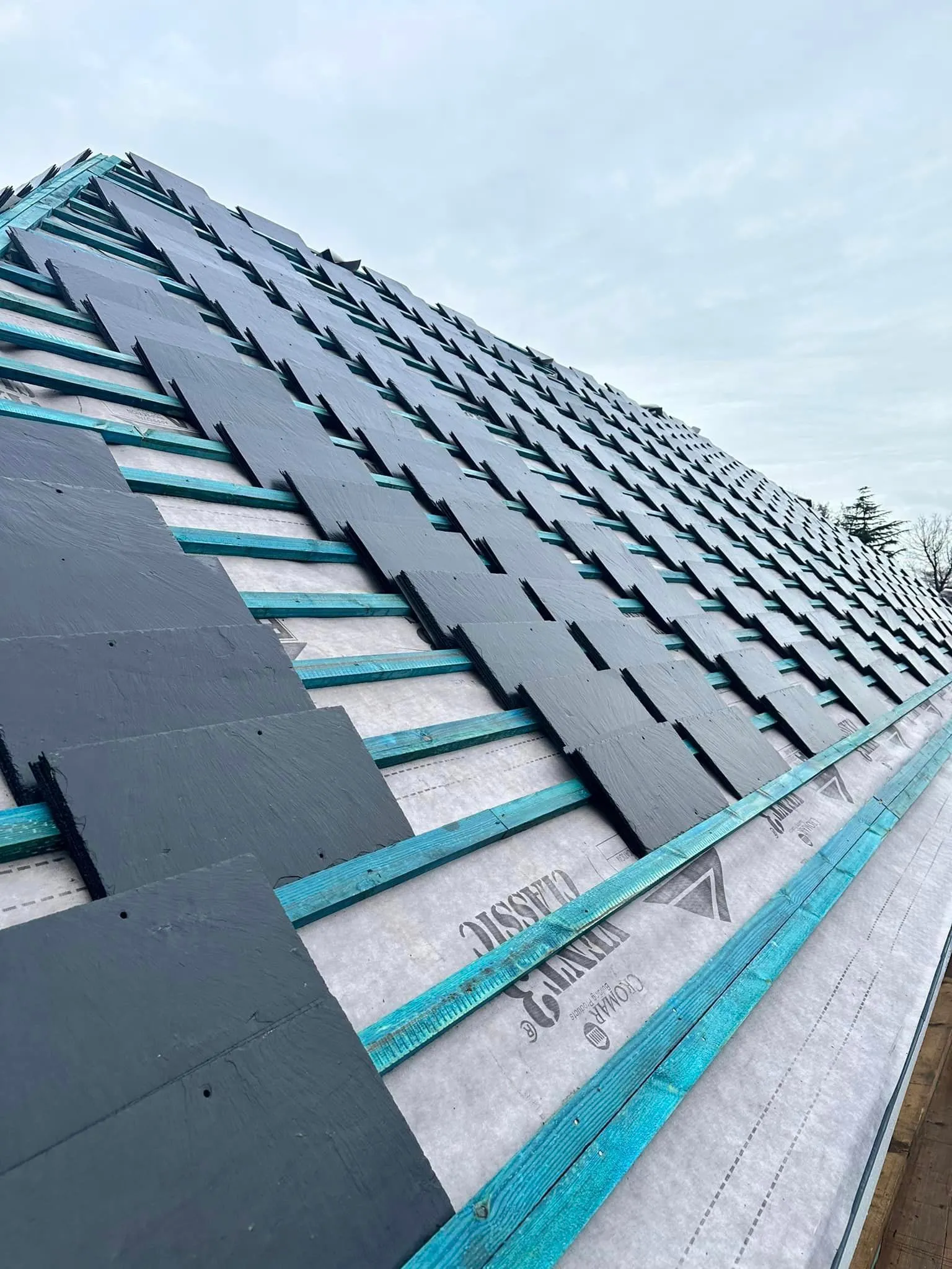 New slate tiles being professionally installed on a pitched roof.