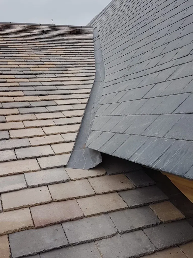 Close-up of a roof valley with curved lead flashing between two different types of roof tiles.