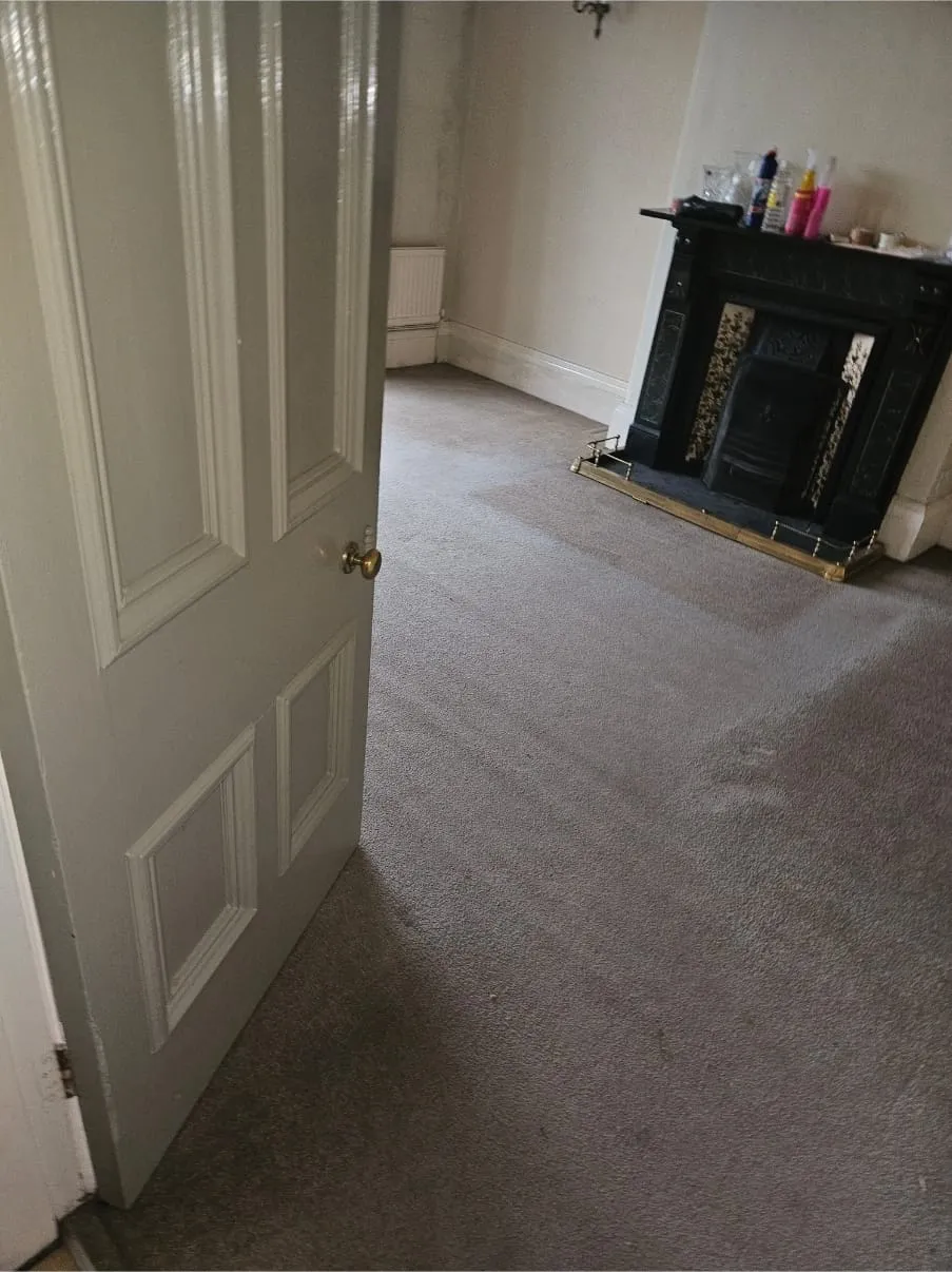 Cleared room with grey carpet and fireplace after house clearance or end-of-tenancy clean