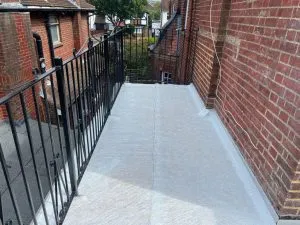 Newly installed flat roof with a light grey membrane and black metal railing on a residential building.