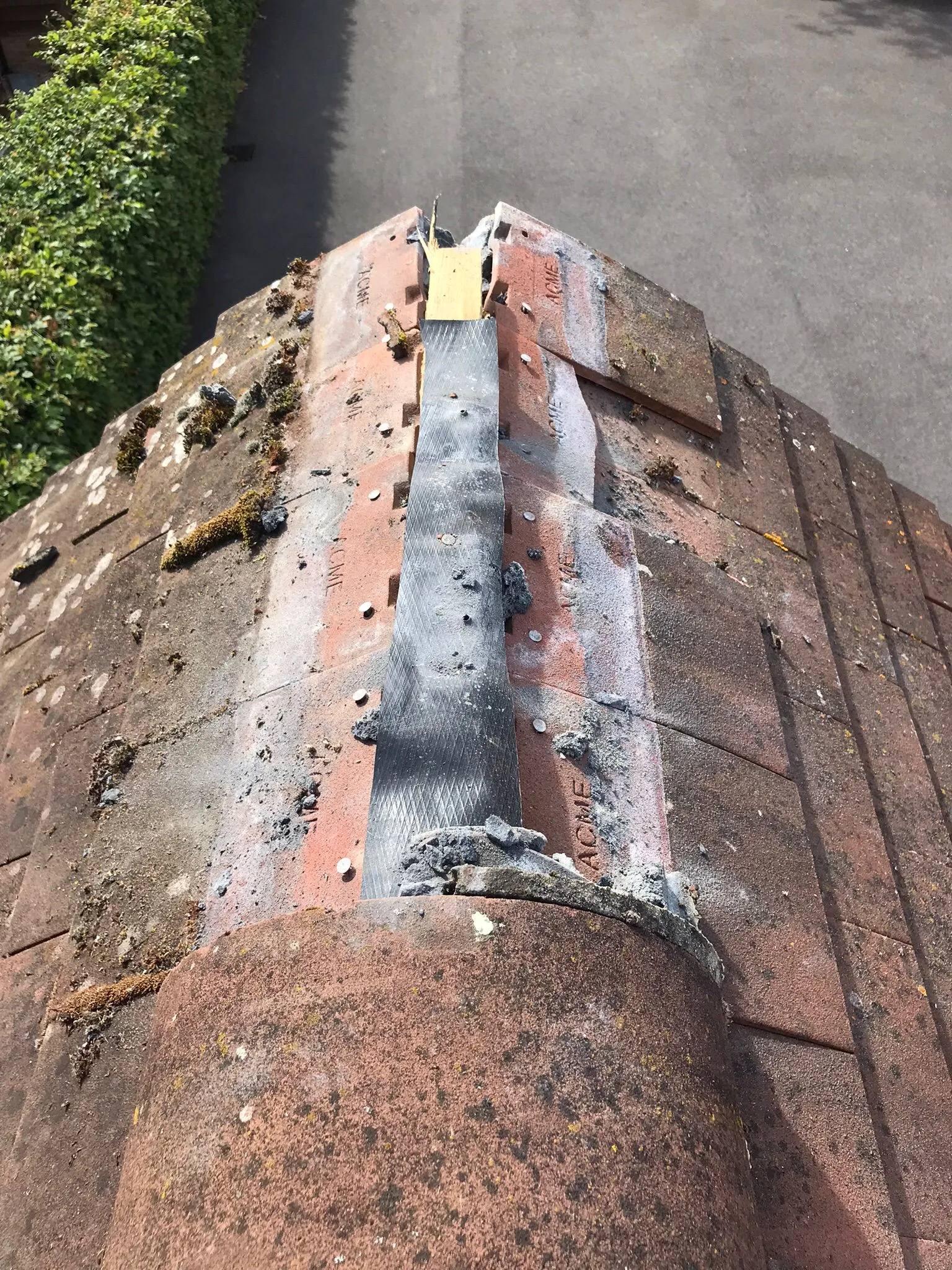 Weathered 'ACME' roof tiles with moss and active ridge repair work under sunny conditions.