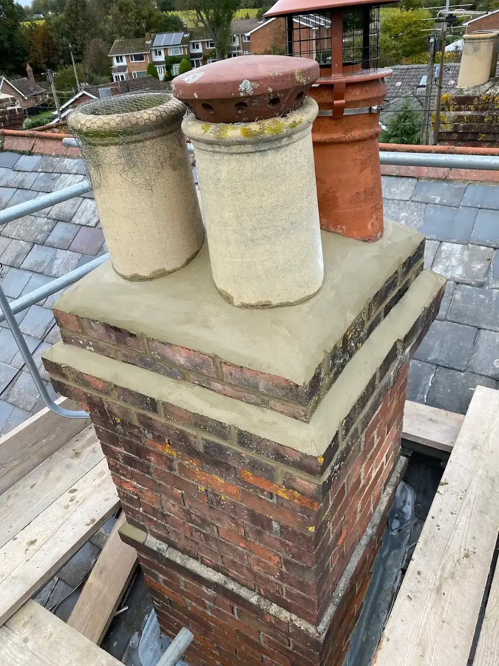 Repaired brick chimney stack with new mortar and chimney pots on a tiled roof.