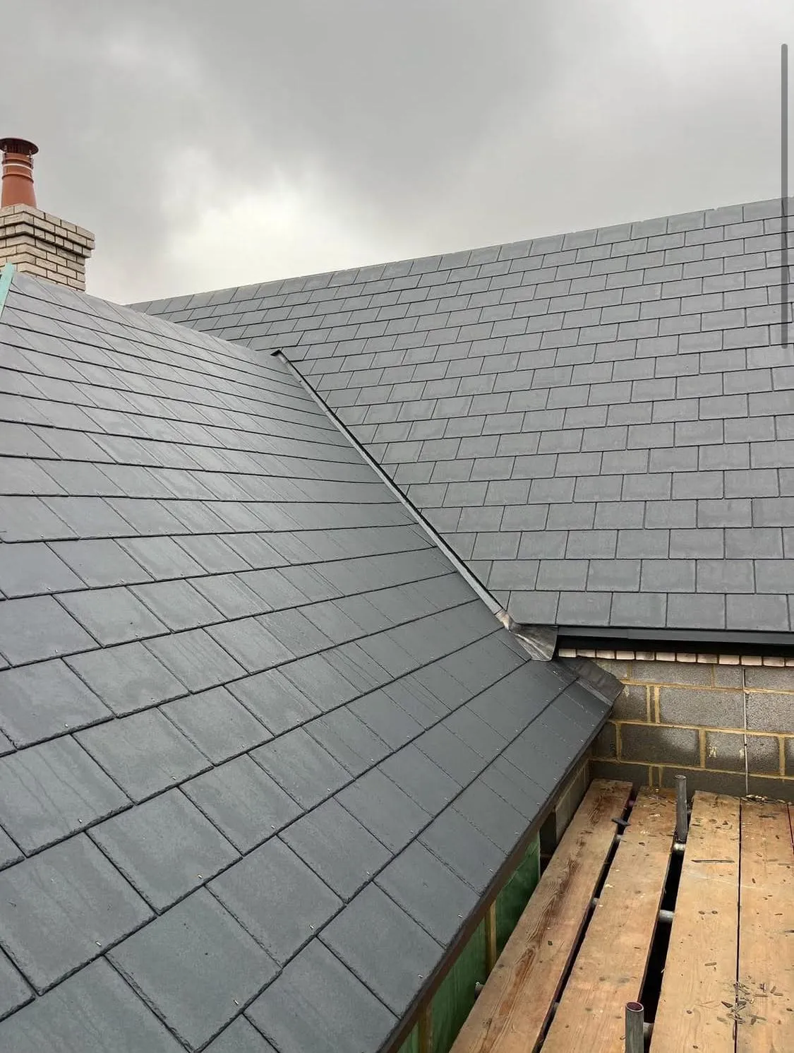 New grey tiled roof installation with chimney and scaffolding by Devon and Cornwall Roofing