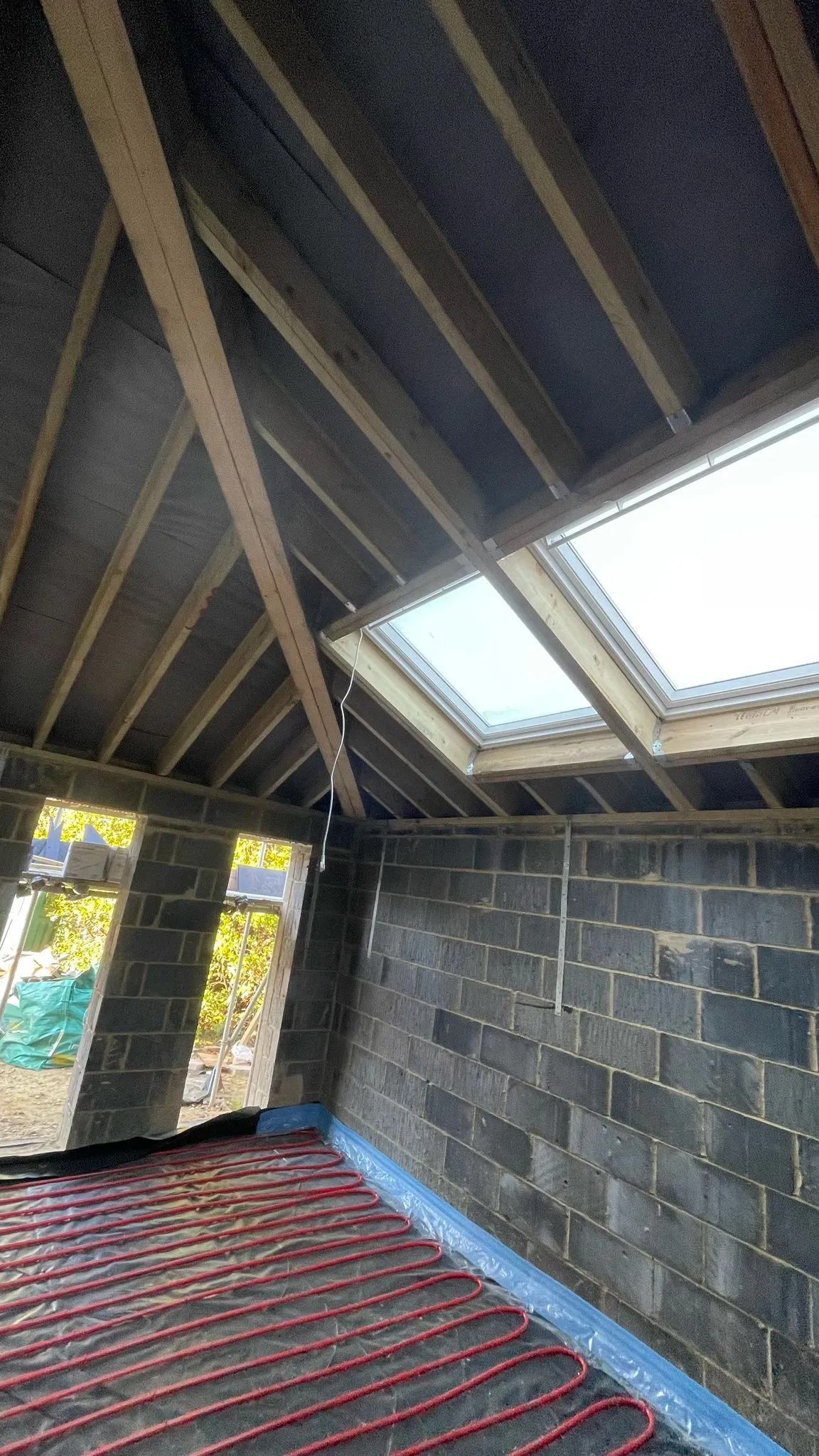 Interior of a home extension project showing first-fix carpentry, roof windows, and underfloor heating installation.