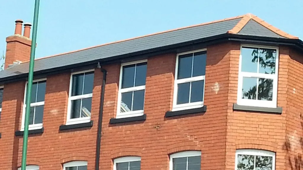 A red brick house with a brand new dark grey tiled pitched roof, new black gutters and fascias, and a chimney stack, reflecting quality roofing work.