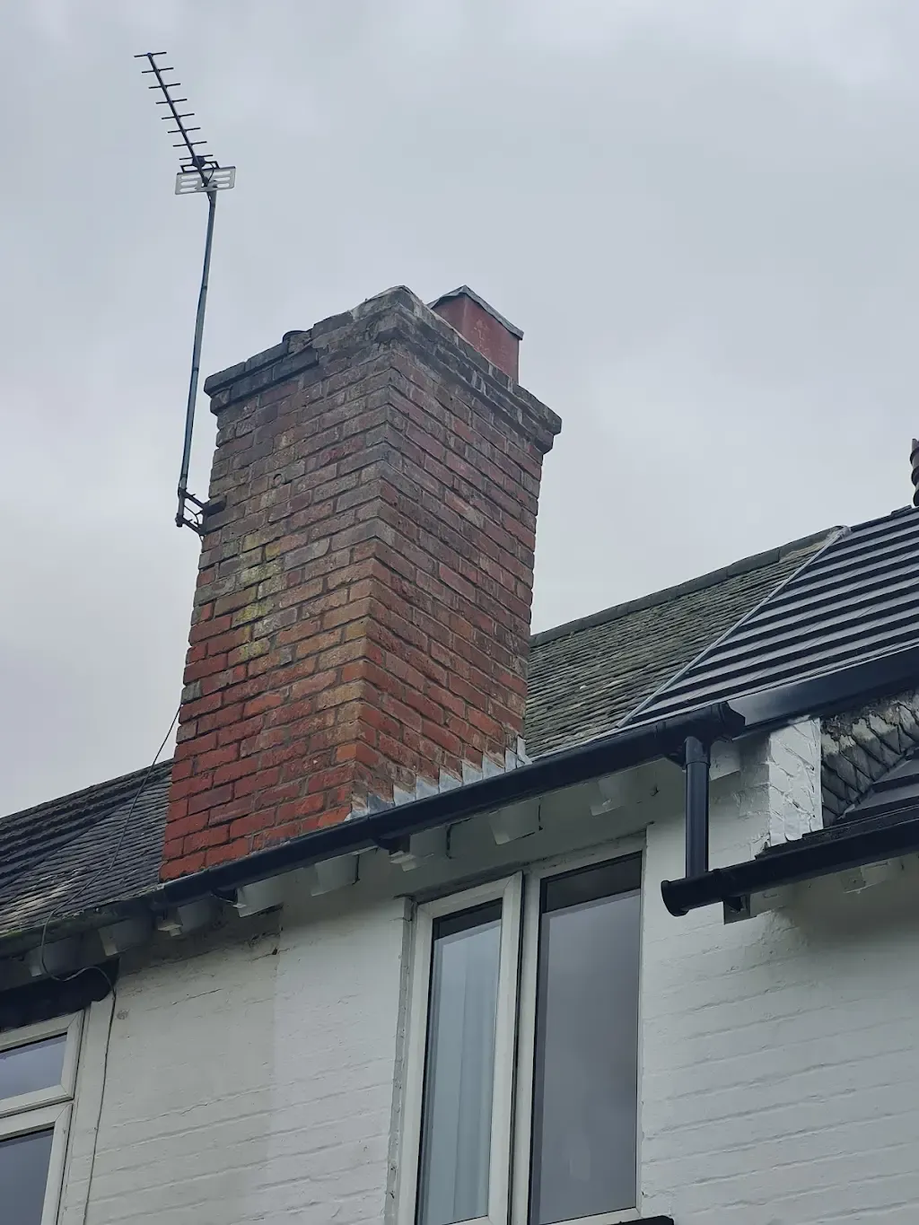 Brick chimney on a house roof with tiled roof and black gutter.