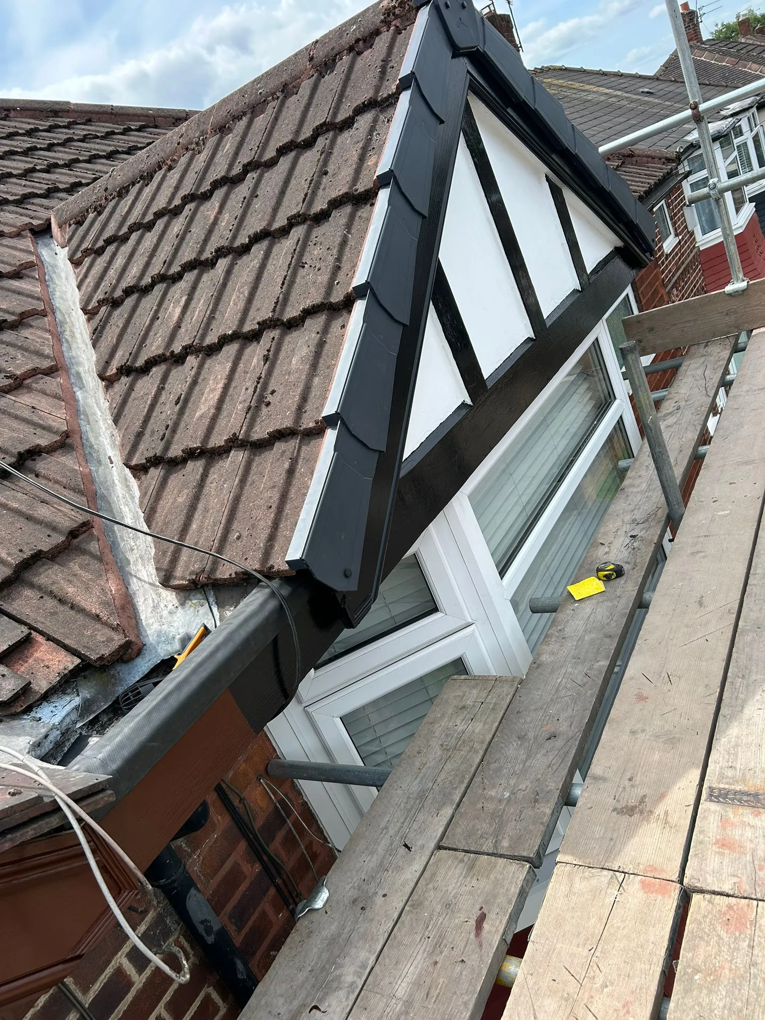 Newly fitted dormer window with black and white exterior on a tiled roof, surrounded by scaffolding.