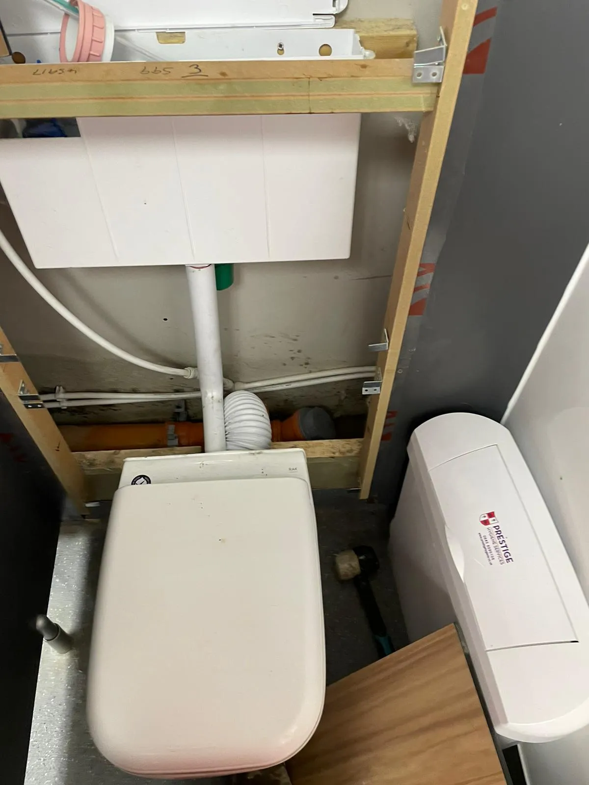Installation of a new toilet system with exposed cistern and drainage pipes in a domestic setting, including a Prestige Hydrocare unit.