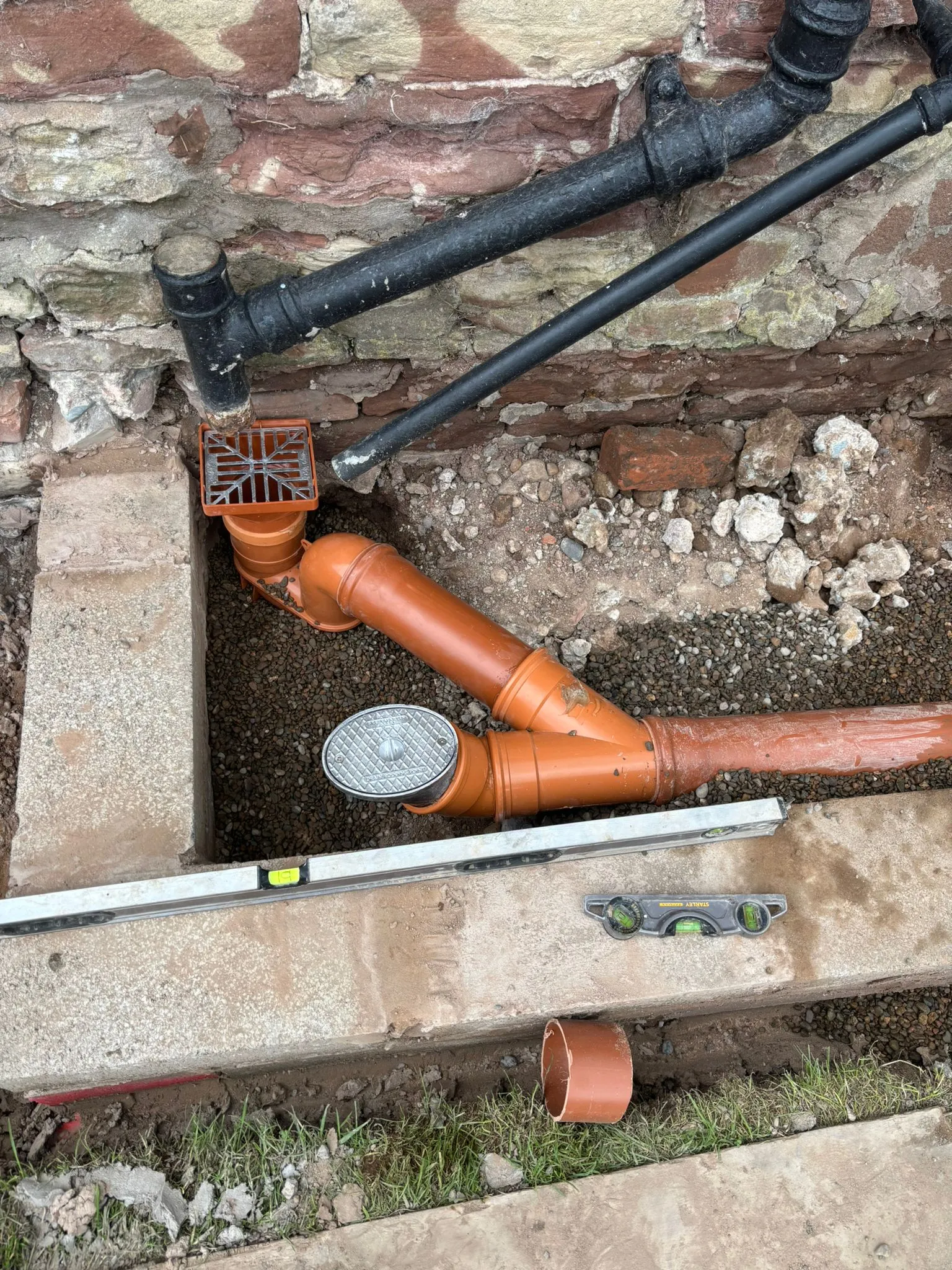 New drainage pipe installation with a gully trap and inspection cover in an excavated trench.