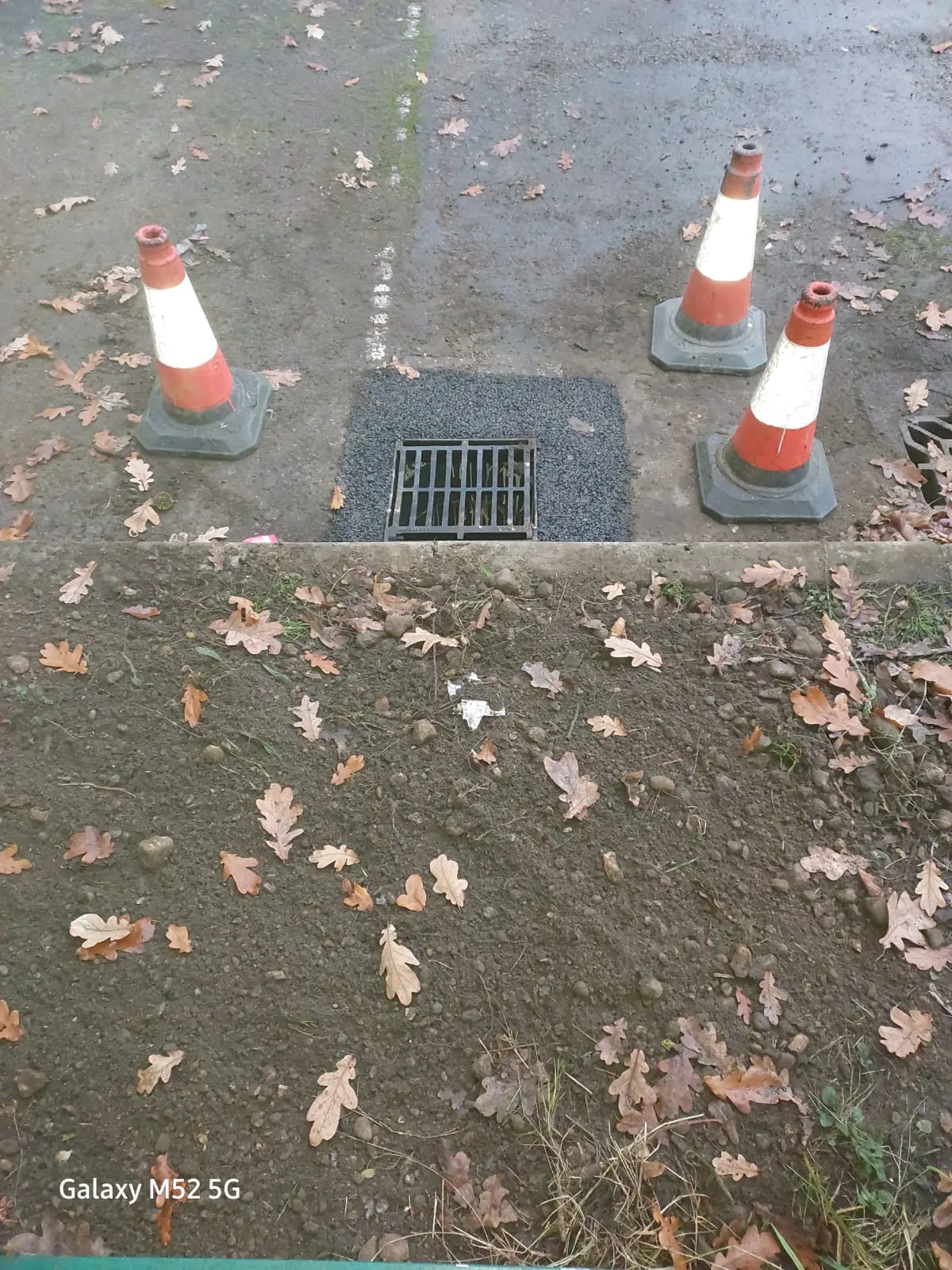 Newly installed storm drain gully with safety cones, indicating recent drainage work.