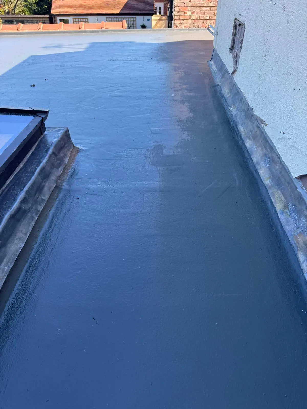 Newly installed dark grey GRP fibreglass flat roof with an integrated skylight and lead flashing.