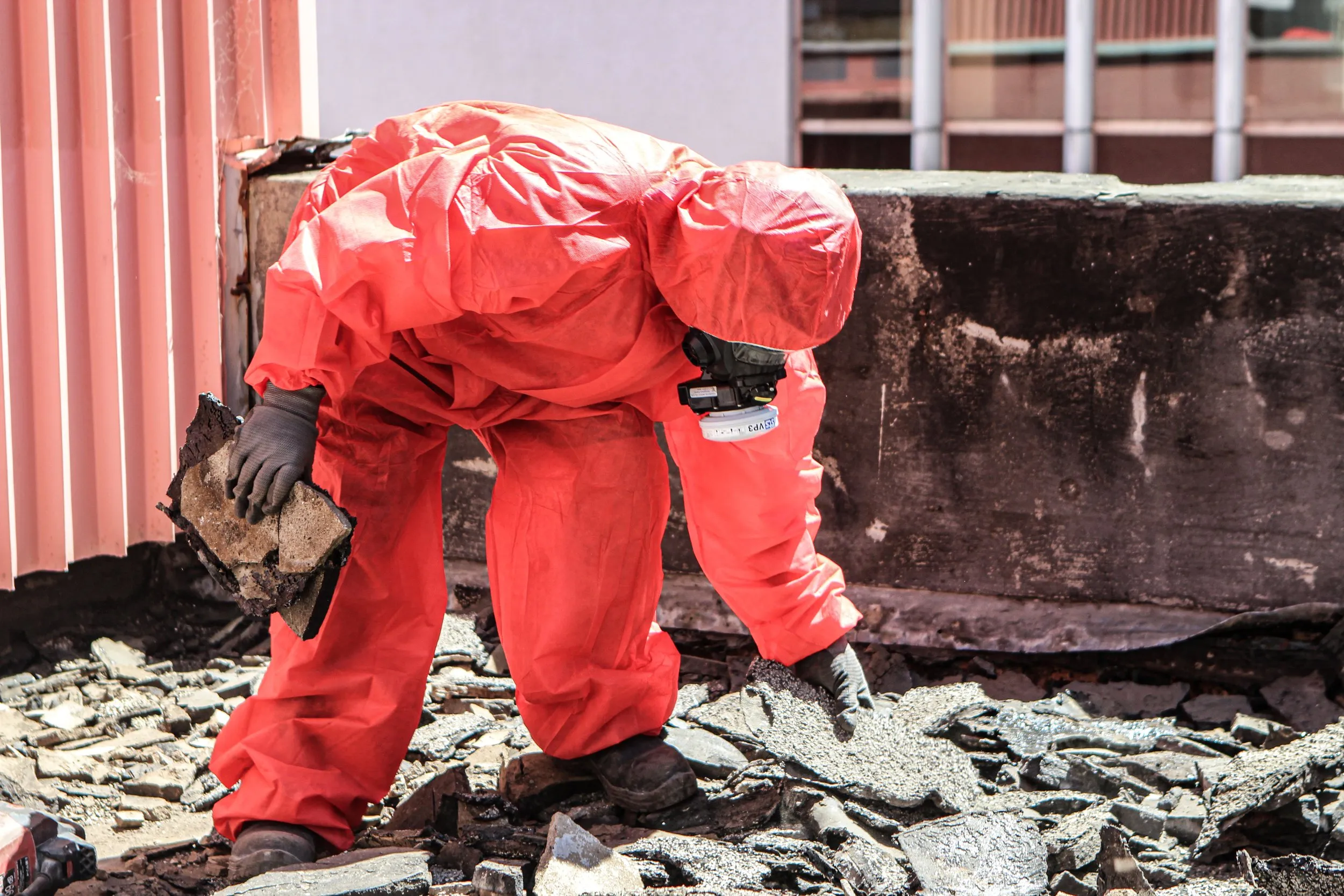 Asbestos surveyor in PPE inspecting debris for asbestos
