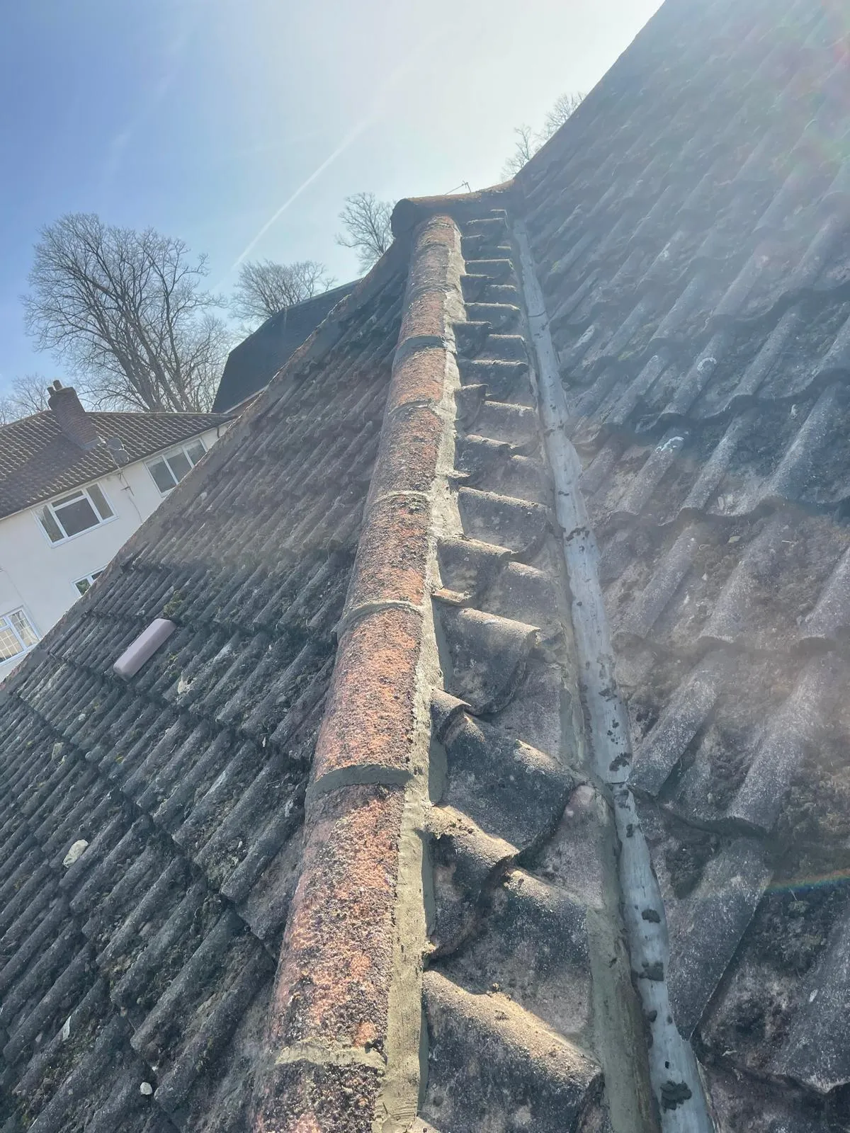An old pitched tiled roof with significant moss on the tiles and a worn valley with what appears to be lead flashing, indicating a need for maintenance or repair.