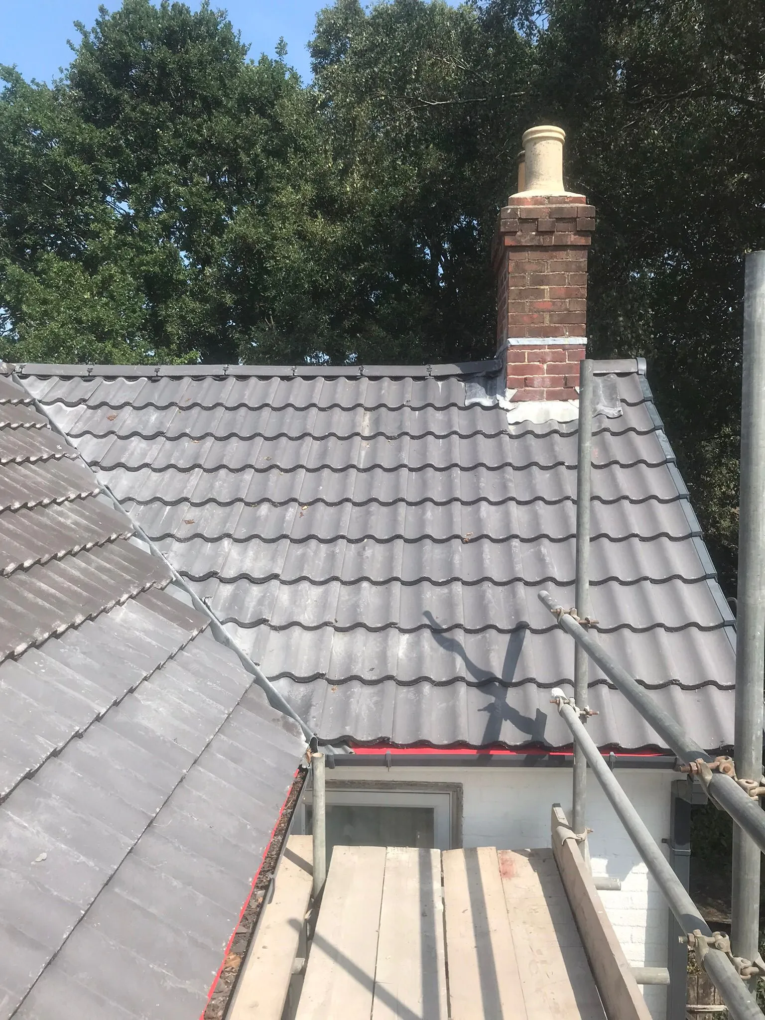 Newly renovated tiled pitched roof with a brick chimney stack and scaffolding