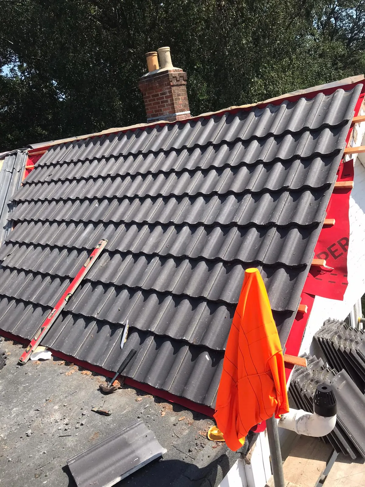 A pitched roof being installed or repaired with new dark grey tiles, red underlay, and a brick chimney visible.
