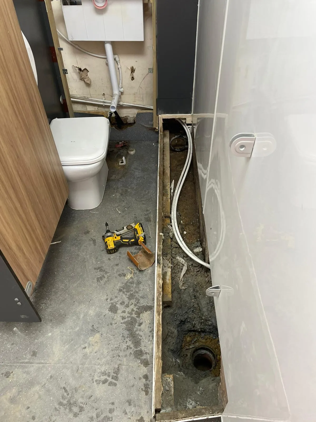 Open floor revealing drainage pipes and a sewer connection in a bathroom under renovation or repair.