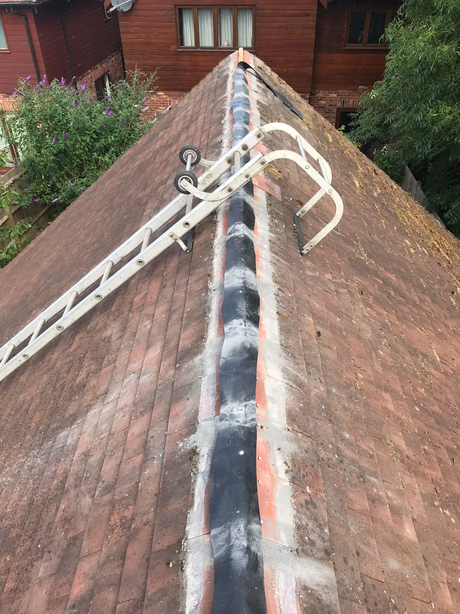 A pitched tiled roof with a ladder, showcasing the ridge and weathered tiles.