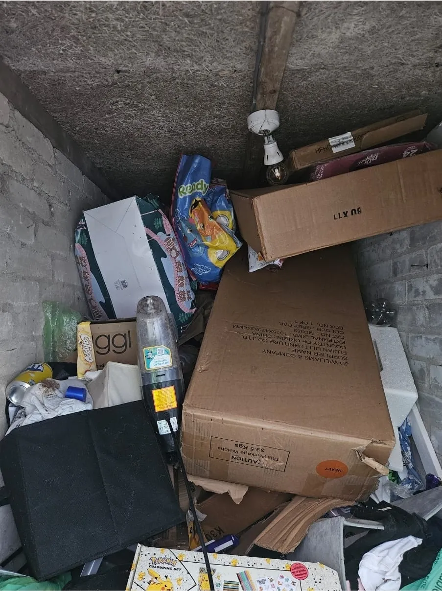 A very cluttered storage space or small room overflowing with boxes, bags, and discarded household items, illustrating a difficult clearance job.