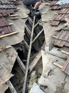 Close-up of a heavily damaged pitched roof valley showing exposed timber joists and missing roofing materials.