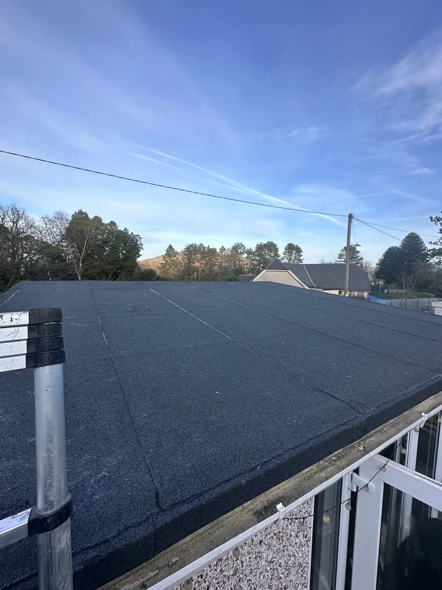 Finished felt flat roof on a residential property under a clear blue sky.