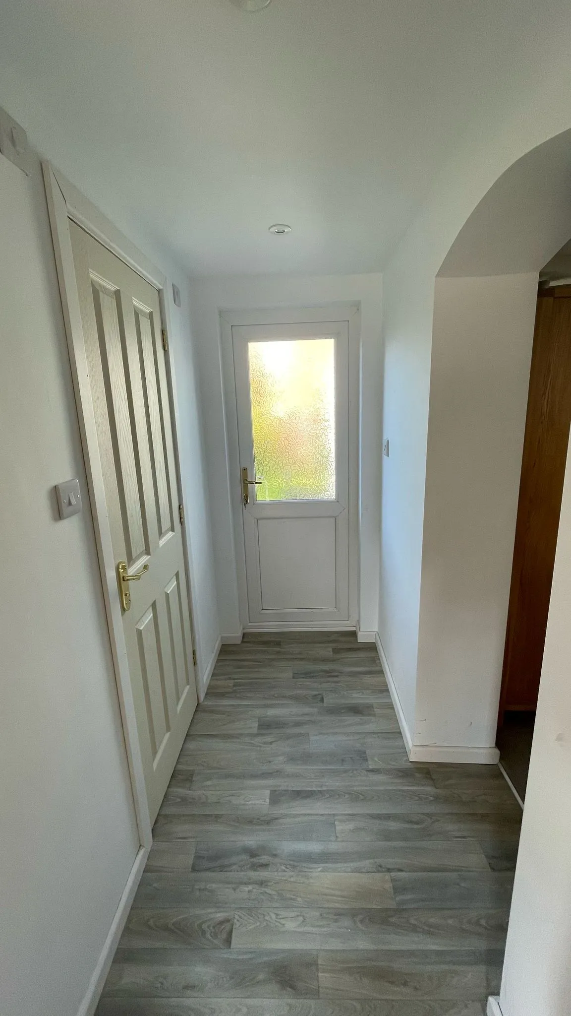 A modernised hallway with grey laminate flooring and a white uPVC door at the end.