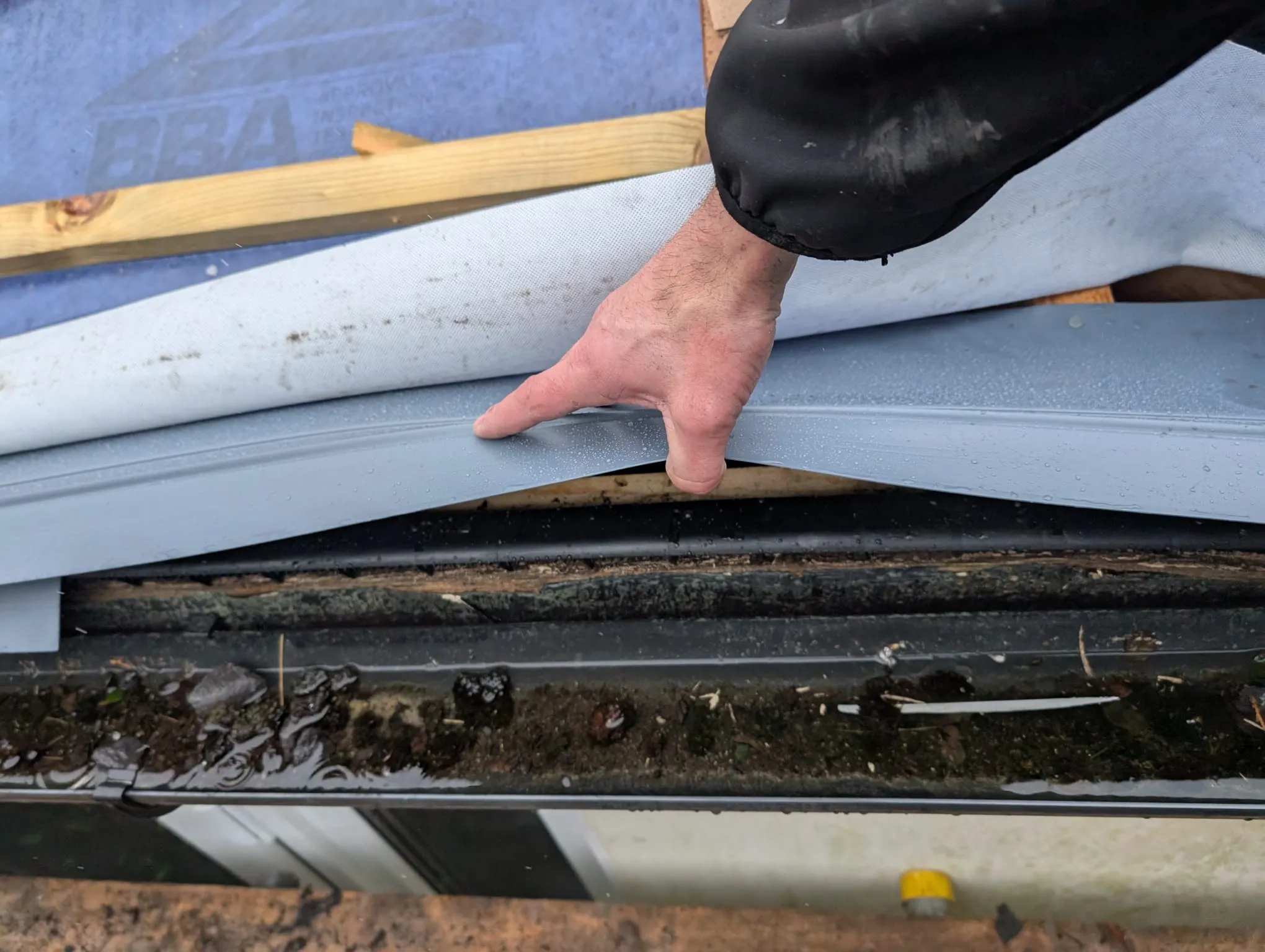 A roofer inspecting a roofline and a blocked gutter.