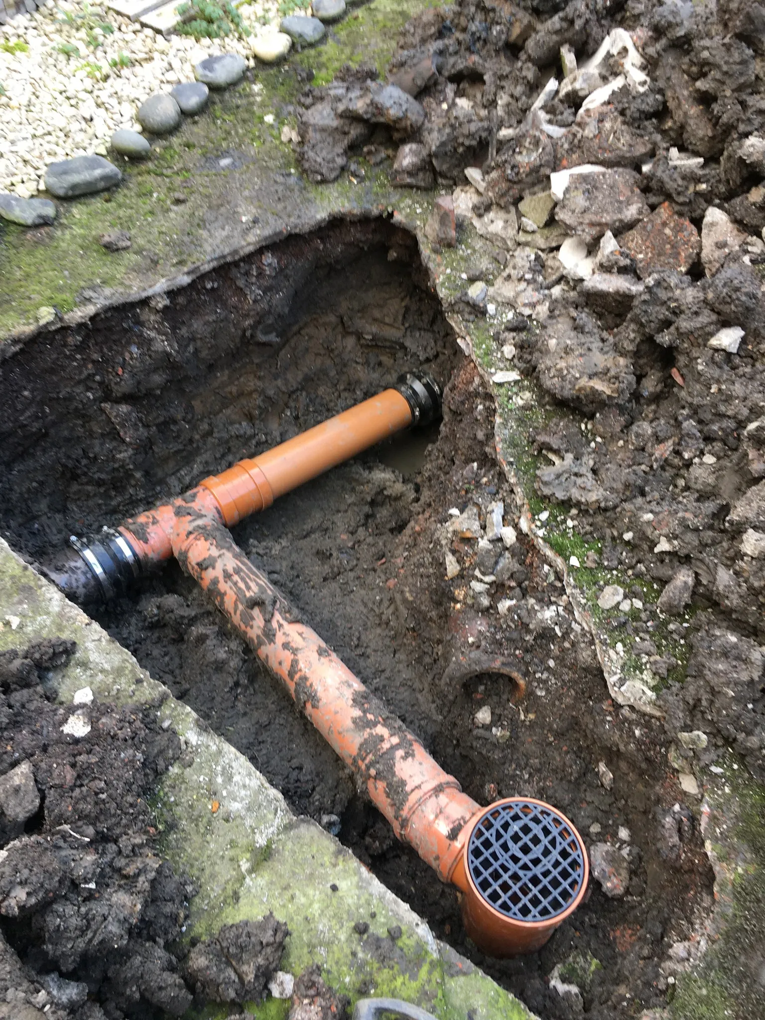 Excavated trench showing orange drainage pipe being laid in the ground
